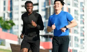 Deux hommes souriants courent ensemble dans un parc urbain. Ils semblent apprécier leur routine de courir tous les jours.