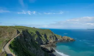 Chemin côtier verdoyant sur les falaises de Jersey, idéal pour visiter Jersey à pied. Mer bleue et ciel clair.