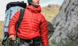 Escaladeur portant une veste rouge en matière doudoune, sac à dos et chaussures d'escalade.