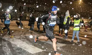 Coureurs de la SaintéLyon affrontant la neige. Un homme porte une lampe frontale et un dossard "Asics".