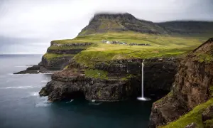 Paysage spectaculaire des îles Féroé : une cascade tombe d'une falaise verdoyante dans l'océan. Idéal pour une randonnée inoubliable.