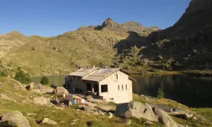 Refuge de montagne au bord d'un lac, idéal pour une randonnée vallée des merveilles 2 jours. Des randonneurs se reposent.
