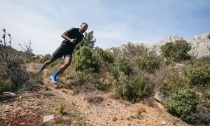 Un coureur en pleine action sur un sentier rocailleux, profitant d'une course à étapes dans un paysage aride et montagneux.