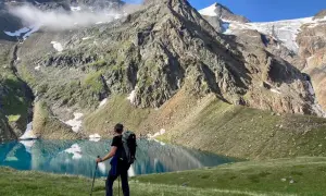 Un randonneur admire un lac turquoise lors d'un trek en Autriche, avec des montagnes imposantes en arrière-plan.
