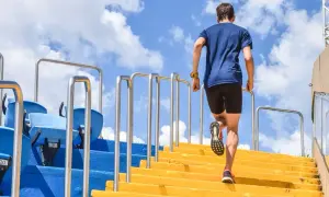 Un homme en tenue de sport monte des escaliers jaunes, un entraînement de renfo course à pied sous un ciel bleu.