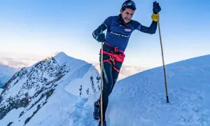 Manuel Merillas, le coureur de trail, franchit une crête enneigée, bâtons en main, sous un ciel bleu éclatant.