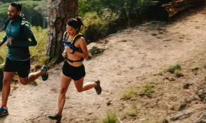 Deux coureurs s'entraînent sur un sentier de montagne, profitant d'un entraînement fractionné trail dans un paysage verdoyant.