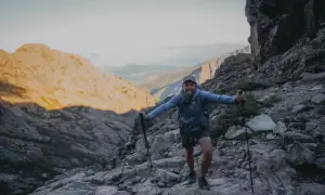 Un randonneur souriant sur un sentier rocheux, bâtons en main. Il semble se demander quel est le gr le plus difficile.