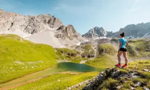Une femme admire un lac de montagne lors d'une randonnée à Courchevel. Paysage alpin spectaculaire avec des montagnes rocheuses et des prairies verdoyantes.