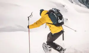 Une personne en raquettes, veste jaune, sac à dos, profite d'une rando raquette Vosges dans un paysage enneigé.