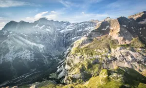Le cirque de Gavarnie, majestueux amphithéâtre naturel, dévoile ses falaises abruptes, une cascade lointaine et des pentes verdoyantes sous un ciel bleu.