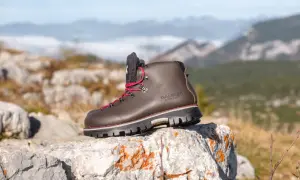 Une bonne chaussure de marche marron, lacets rouges, sur un rocher, avec des montagnes brumeuses en arrière-plan.
