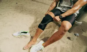 Un athlète ajuste sa genouillère TFL Decathlon sur un terrain sablonneux, prêt pour son entraînement.