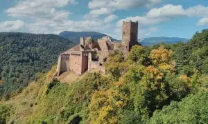 Les 3 châteaux de Ribeauvillé, perchés sur une colline boisée, se dressent fièrement sous un ciel bleu parsemé de nuages.