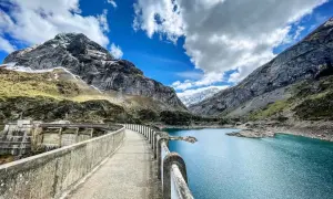 Le cirque de Gavarnie lac, un barrage imposant domine un lac bleu turquoise, entouré de montagnes majestueuses sous un ciel nuageux.