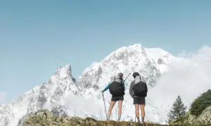 Deux randonneurs, prêts pour une randonnée de 3 jours, contemplent un paysage montagneux enneigé sous un ciel bleu.