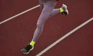 Une athlète court sur une piste, portant une chaussure de marche longue distance et des chaussettes fluo.