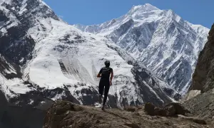 Perrine Fages court sur un sentier rocailleux face à des montagnes enneigées majestueuses sous un ciel bleu éclatant.