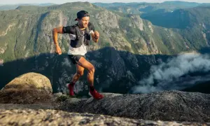 Mathieu Blanchard court sur un sentier rocheux avec des montagnes verdoyantes en arrière-plan.