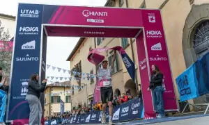 Un coureur franchit la ligne d'arrivée du Chianti by UTMB, acclamé par la foule. Il tient une banderole rose de finisher.