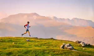 Un coureur en plein effort sur un sentier de montagne, prêt pour une ultra trail distance. Le soleil couchant illumine le paysage.