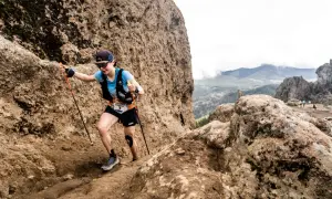 Katharina Hartmuth grimpe un sentier rocheux escarpé, bâtons en main, lors d'une course en montagne.