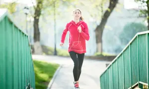 Une jeune femme en tenue de sport court sur un chemin bordé de verdure. Elle semble apprécier son activité, peut-être pour courir 20 minutes par jour.