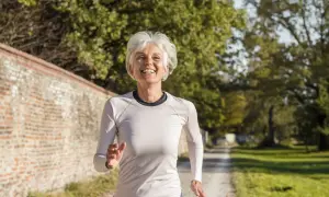 Femme souriante de 60 ans courant sur un chemin, suivant un plan d'entraînement course à pied.