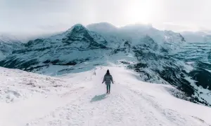 Une personne marche sur un sentier enneigé, dominant des montagnes majestueuses. Un paysage hivernal à couper le souffle, typique d'Interlaken, Suisse.