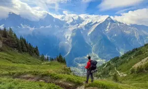 Randonneur contemplant les majestueuses montagnes enneigées, un paysage digne des **Vosges** en été.