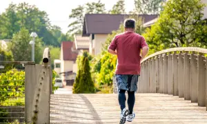 Un homme court sur un pont en bois, profitant du soleil matinal. C'est le meilleur moment pour courir, avec l'air frais et la nature verdoyante.