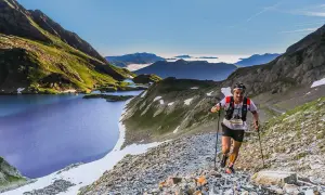 Un coureur de trail, le **vo2 max** à son apogée, grimpe un sentier rocailleux près de lacs de montagne bleus sous un ciel clair.