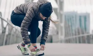 Une femme en tenue de running hiver attache ses lacets sur un pont.