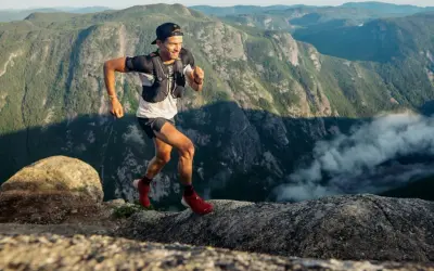 Mathieu Blanchard court sur un sentier rocheux avec des montagnes verdoyantes en arrière-plan.