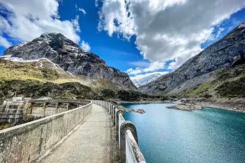 Le cirque de Gavarnie lac, un barrage imposant domine un lac bleu turquoise, entouré de montagnes majestueuses sous un ciel nuageux.