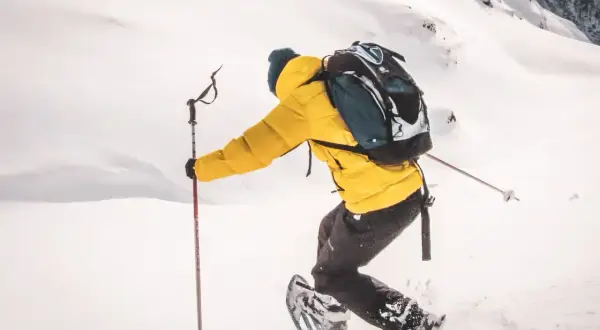Une personne en raquettes, veste jaune, sac à dos, profite d'une rando raquette Vosges dans un paysage enneigé.