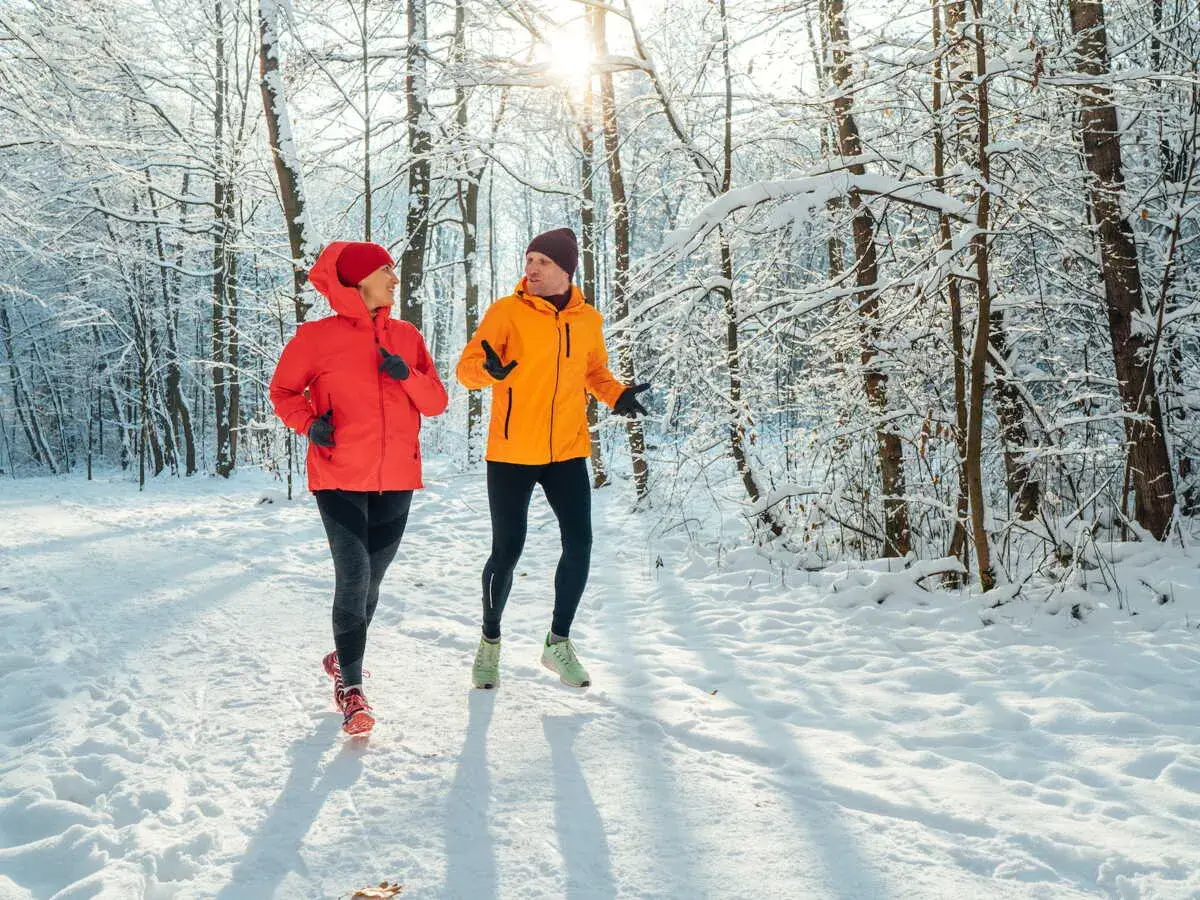 Un couple profite de l'air frais en courant sous la neige dans une forêt enneigée.