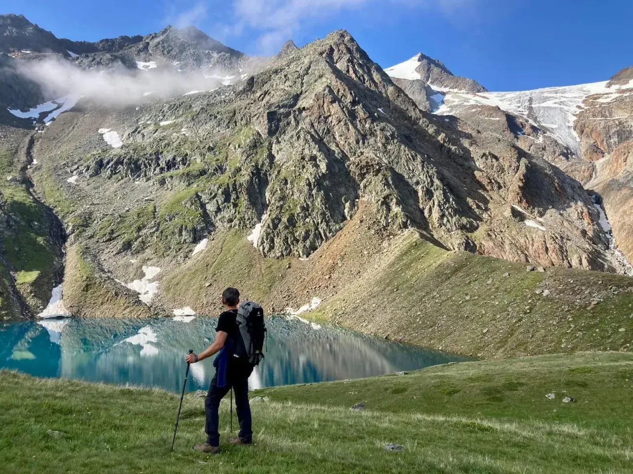 Un randonneur admire un lac turquoise lors d'un trek en Autriche, avec des montagnes imposantes en arrière-plan.