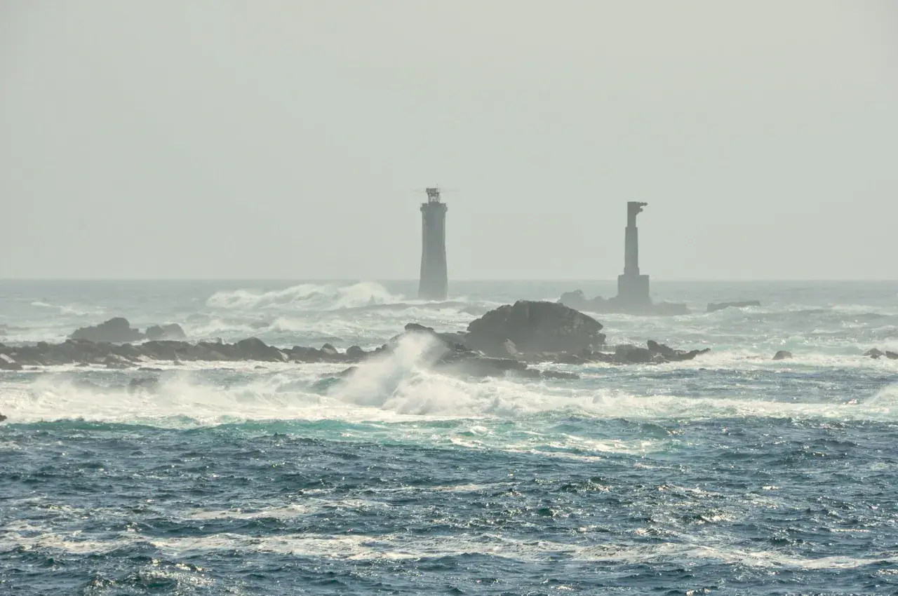 Deux phares se dressent sur des îlots rocheux battus par les vagues, au large de l'île d'Ouessant.