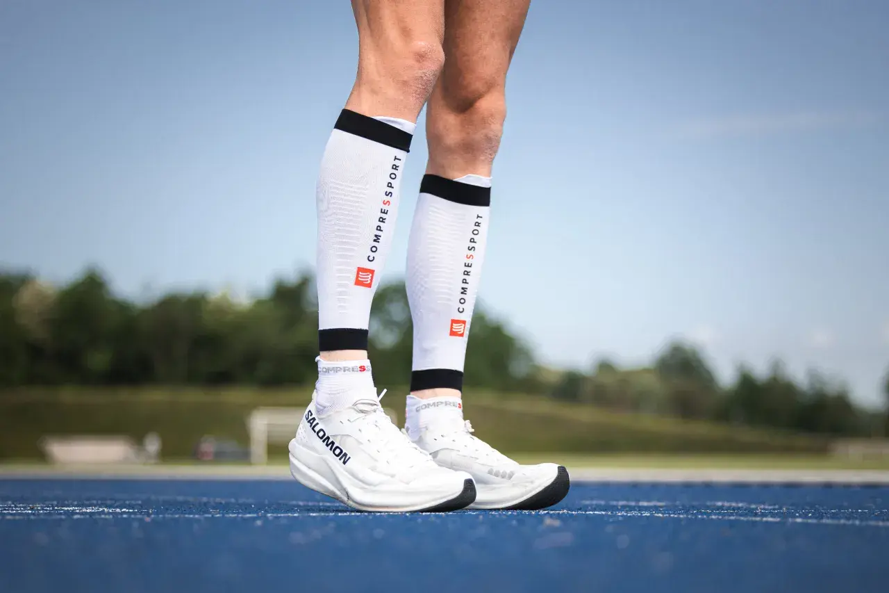 Manchons de compression mollet : pour une meilleure récupération et performance. Ces manchons blancs avec logo Compressport sont portés par un coureur.