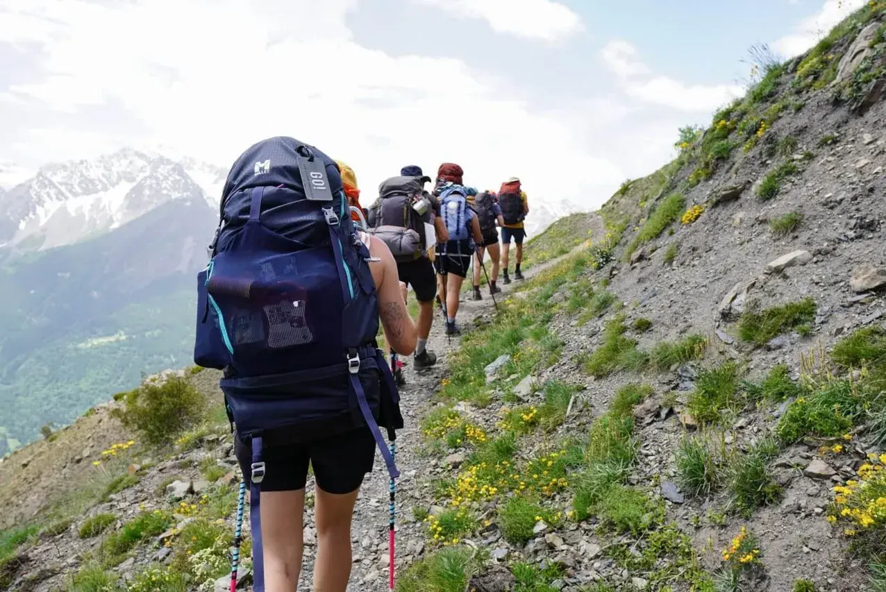 Groupe de randonneurs avec de gros sacs à dos sur un sentier de montagne. Le mot "GO!" est visible sur un sac.
