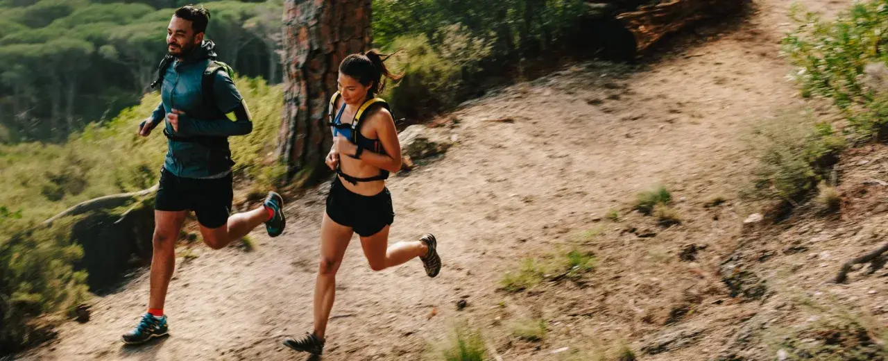 Deux coureurs s'entraînent sur un sentier de montagne, profitant d'un entraînement fractionné trail dans un paysage verdoyant.