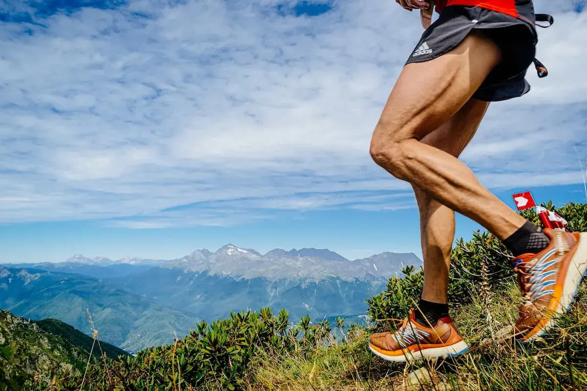 Un coureur en pleine descente trail sur un sentier de montagne, avec des sommets enneigés en arrière-plan.