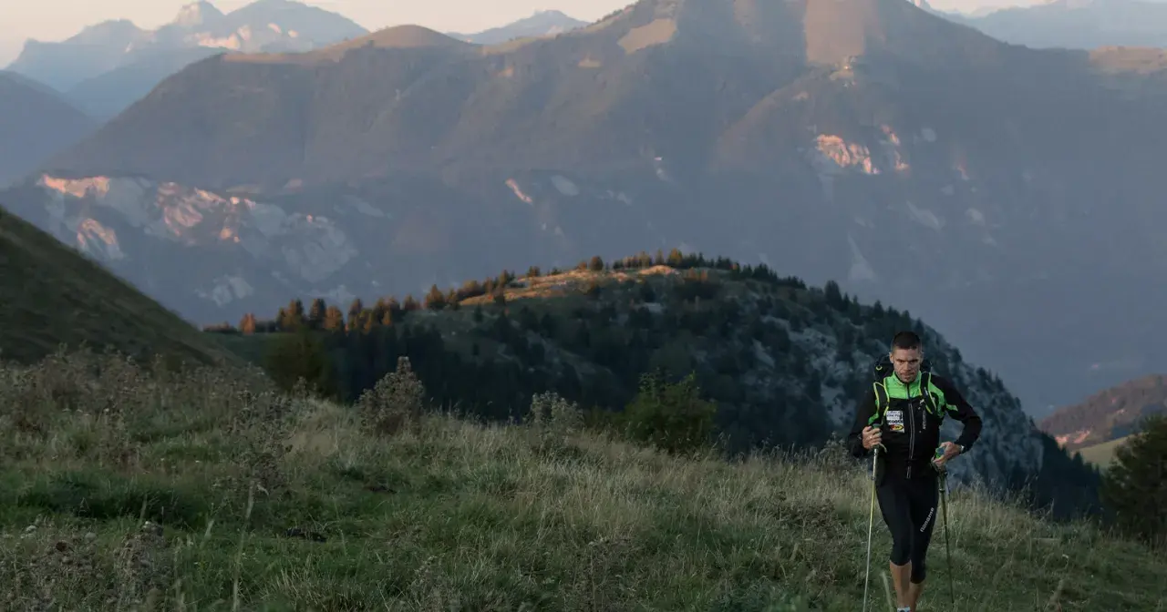 Un coureur en plein effort, bâtons en main, sur un sentier de montagne. Un aperçu de son plan d'entraînement UTMB.