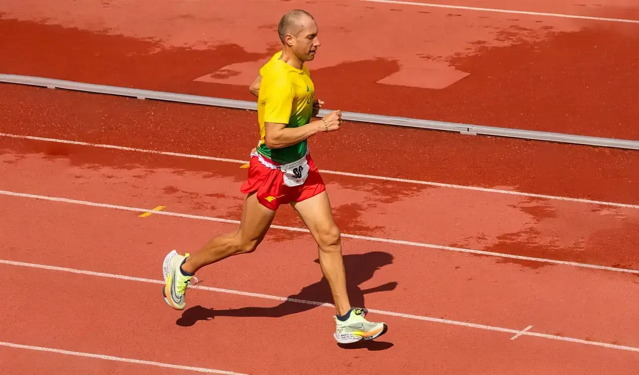 Un athlète en tenue jaune et rouge court sur une piste mouillée, visant le record du monde de vitesse à pied.