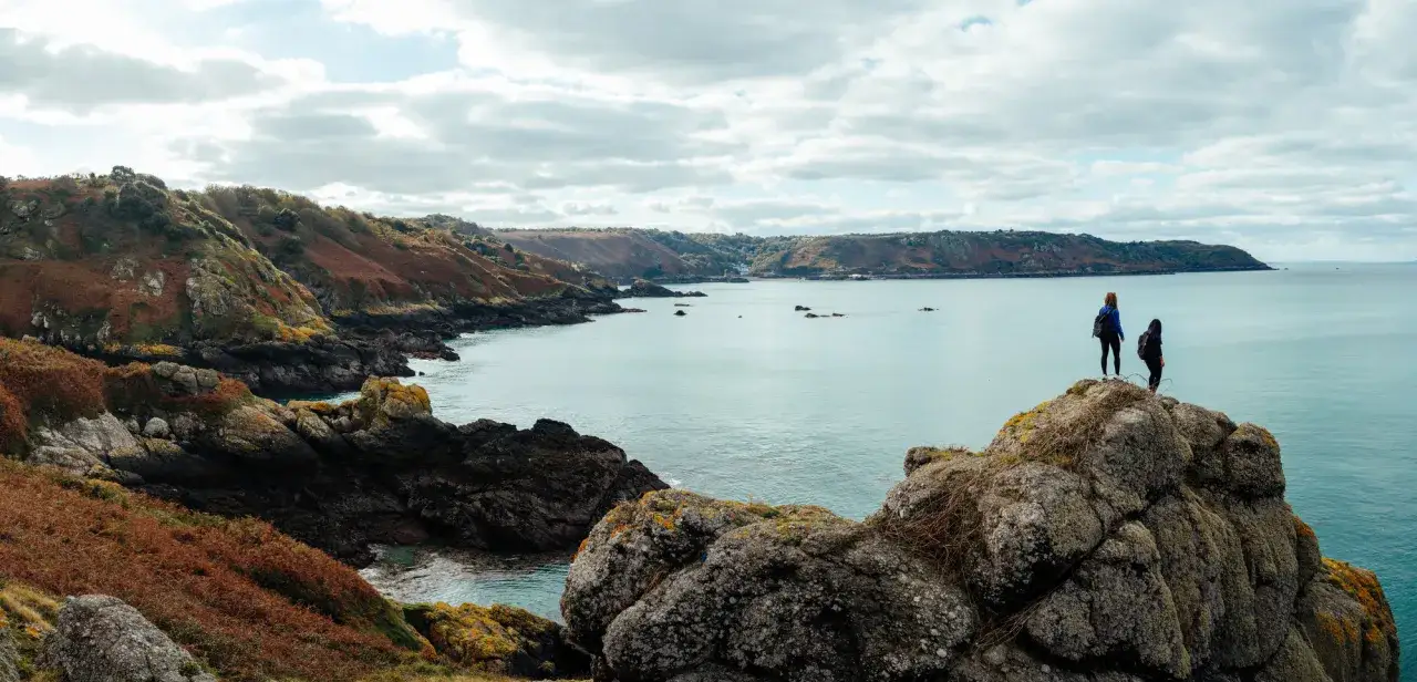Deux randonneuses contemplent la c&ocirc;te rocheuse et la mer lors d'une excursion pour visiter Jersey &agrave; pied.