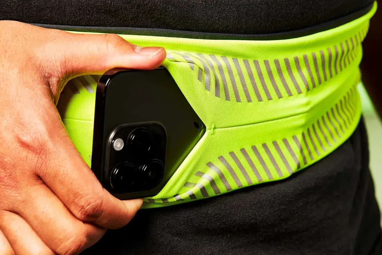 Une main glisse un smartphone dans une ceinture de course fluo. La solution id&eacute;ale pour savoir o&ugrave; mettre son t&eacute;l&eacute;phone quand on court.