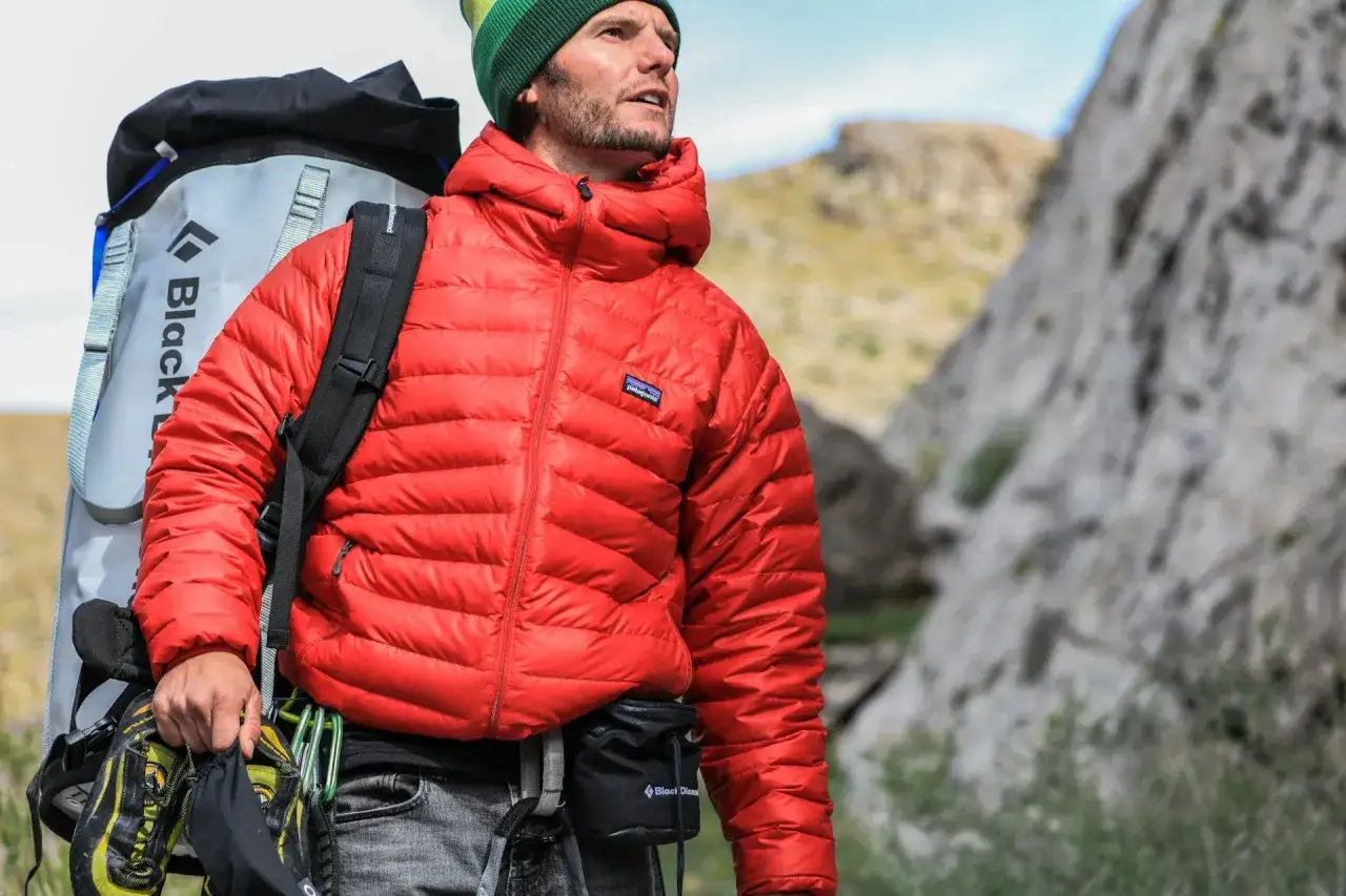 Un alpiniste porte une veste rouge en matière doudoune, un sac à dos Black Diamond et des chaussures d'escalade.