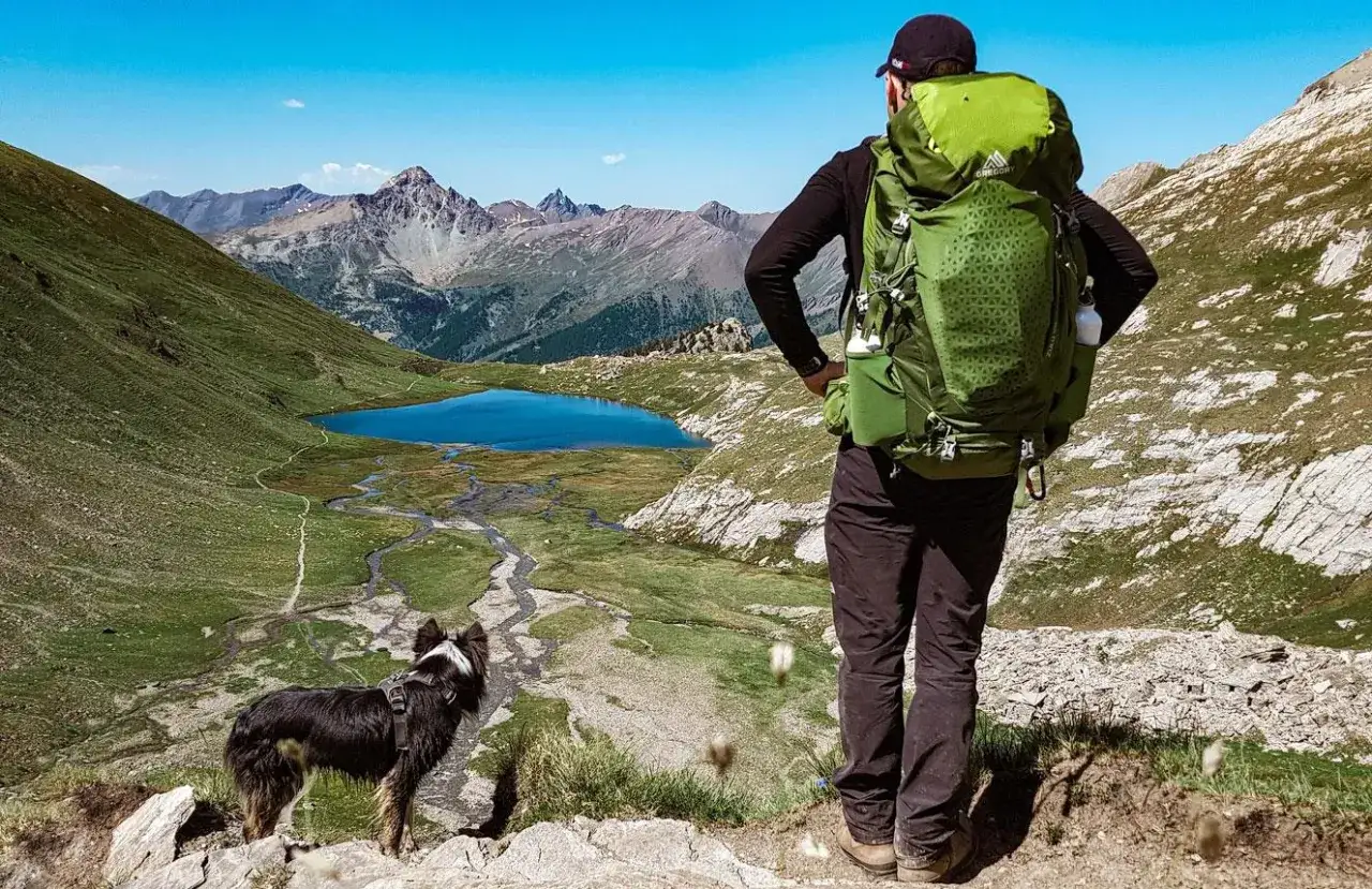 Un homme et son chien profitent d'une vue imprenable sur un lac de montagne lors d'une randonn&eacute;e.