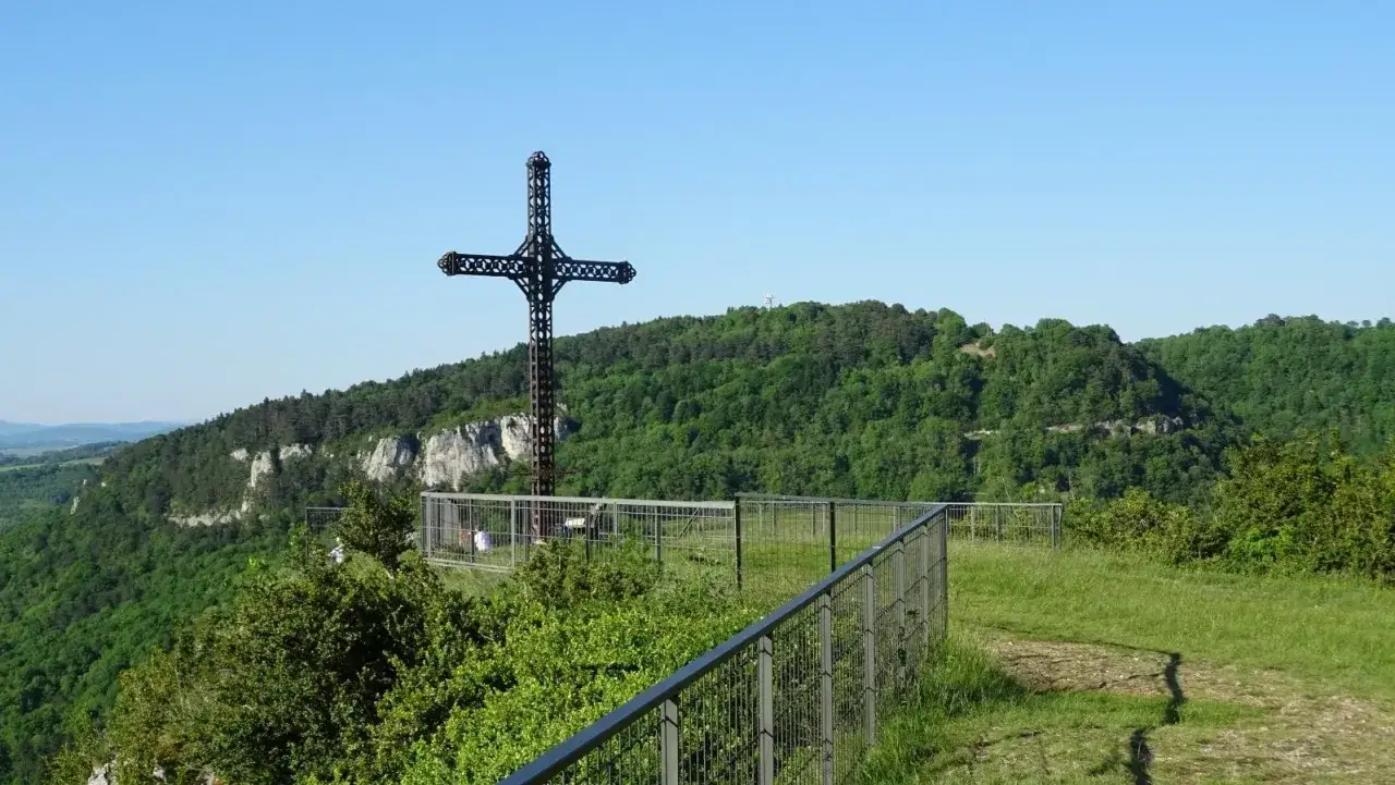La croix du Dan domine un paysage verdoyant. Une cl&ocirc;ture m&eacute;tallique entoure le site, offrant une vue imprenable sur les falaises et la for&ecirc;t.